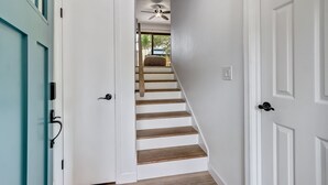 Una escalera con paredes blancas y escalones de madera que conduce a una habitación con ventilador de techo.