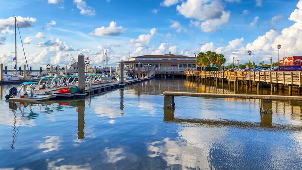 Un puerto deportivo con barcos amarrados, un muelle con asientos de madera y un edificio con un techo amplio.