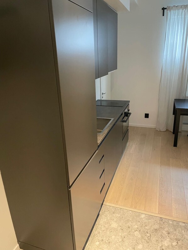A modern kitchen with a dark-colored refrigerator, a built-in oven, and a wooden countertop.