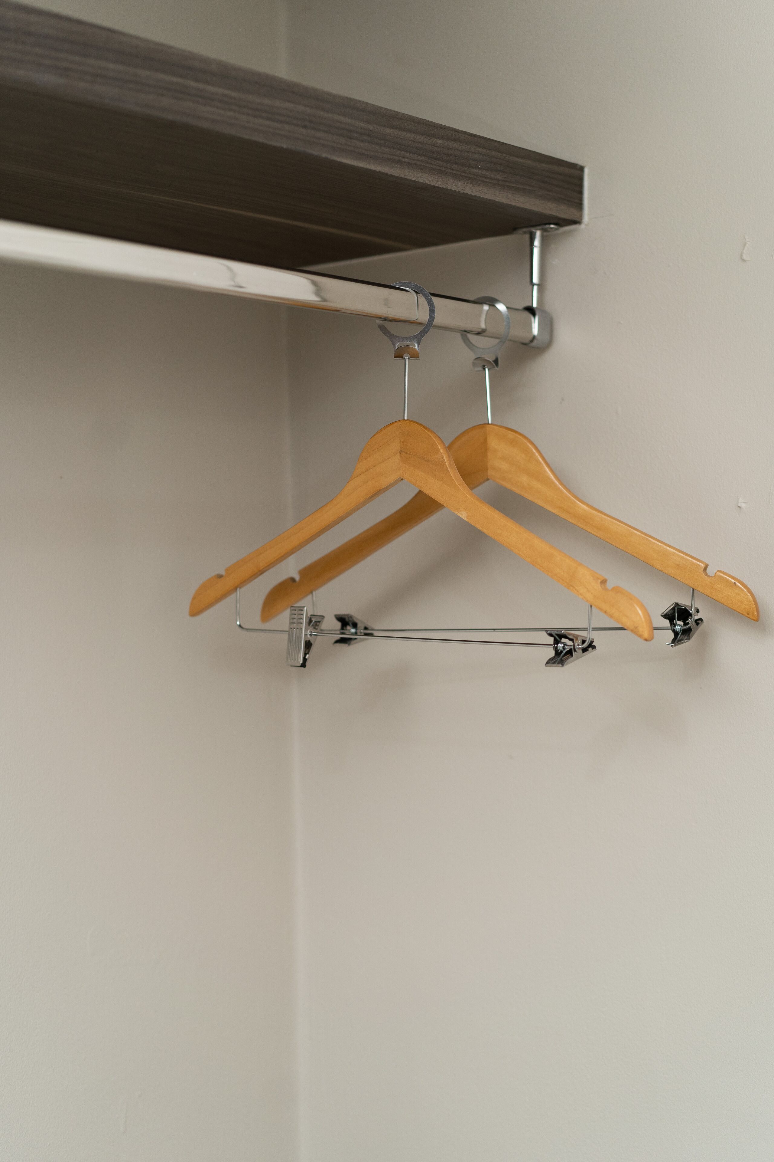 A wooden hanger rack mounted on a wall with a metal shelf above it.