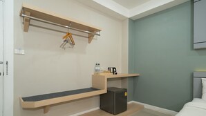 Habitación de hotel compacta con cama, un pequeño escritorio con hervidor, refrigerador y repisa de madera con objetos colgando.