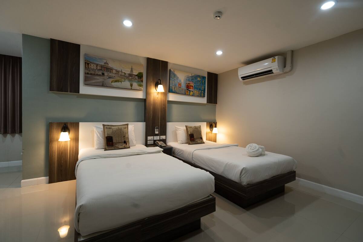 A hotel room with two beds, a wall-mounted air conditioner, and artwork above the beds.