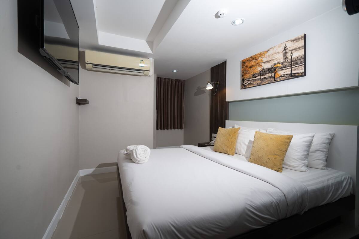 A hotel room with a large bed, a painting on the wall, a ceiling fan, and an air conditioning unit.