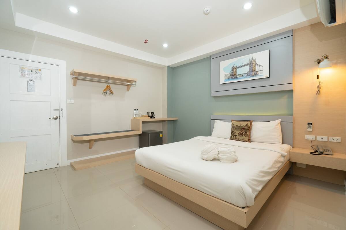 A modern hotel room with a bed, a bedside table, a wall-mounted shelf, and a painting of a bridge.