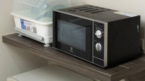 Un horno microondas en un estante con un recipiente de plástico y una tetera.