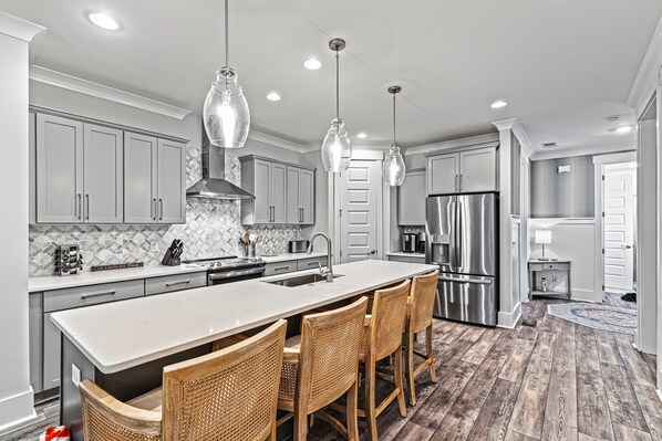 A modern kitchen with a large island, stainless steel appliances, and wicker bar stools.