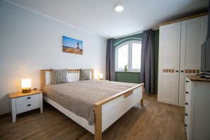 Une chambre à coucher comprenant un lit, des tables de chevet, une fenêtre avec des rideaux, une armoire et un tableau accroché au mur.
