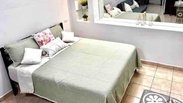 A bedroom with a bed, a large mirror, and a small table with a lamp. - Loft in the Heart of La Paz. 5 Blocks to Malecon Street (La Paz)