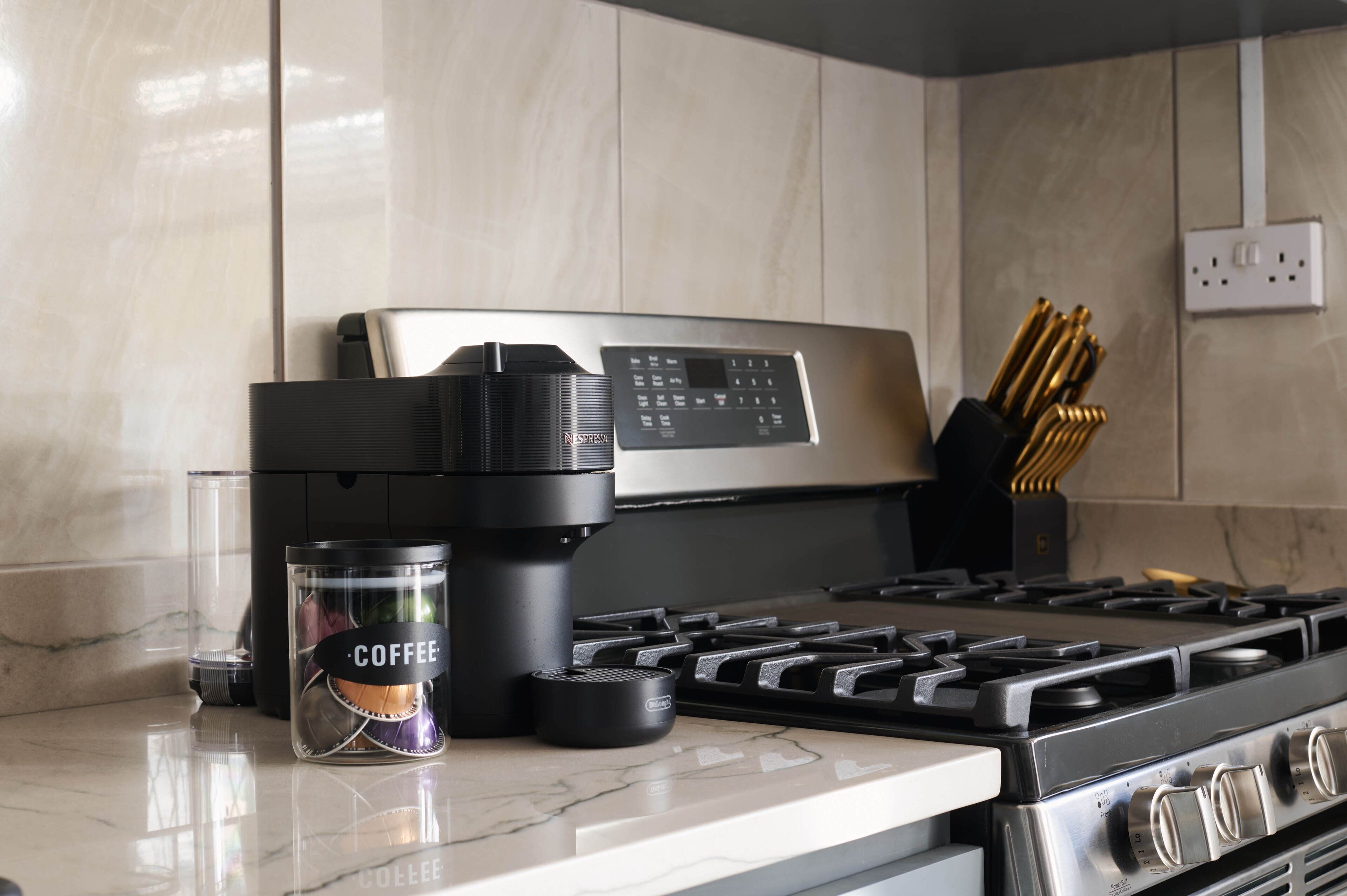 A kitchen with a stainless steel stove, a coffee maker, and a glass container labeled "COFFEE" on the counter.