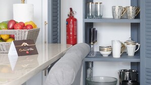 Un espace cuisine bien organisé, avec un meuble gris contenant divers ustensiles de cuisine, un panier en osier rempli de fruits et un extincteur.