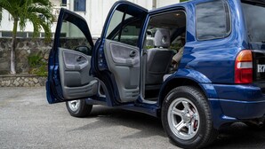 Un VUS bleu, avec les portes arrière ouvertes, est garé dans une rue.