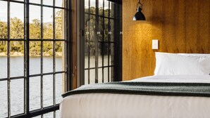 Habitación de hotel con un amplio ventanal que ofrece vista a un cuerpo de agua y árboles.