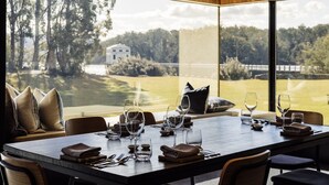 Comedor con una mesa grande preparada para cuatro personas, ventanas amplias que ofrecen vistas a un campo de golf y un edificio a lo lejos.