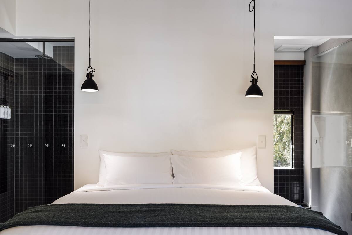 Un dormitorio moderno con una cama grande, dos lámparas colgantes y vistas a un baño con azulejos negros.