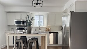 A modern kitchen with white cabinets, stainless steel appliances, a wooden island with bar stools, and a large refrigerator.