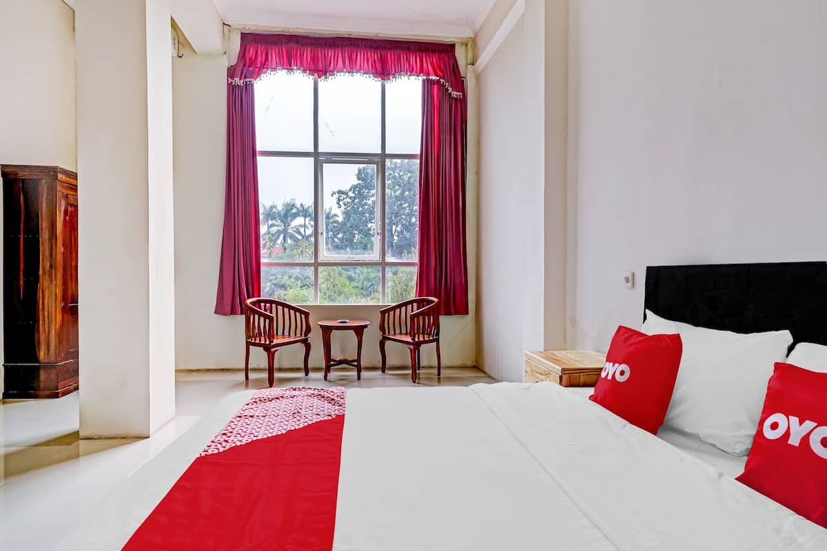 A hotel room with a bed, a window with curtains, a small table with chairs, and a wooden cabinet.