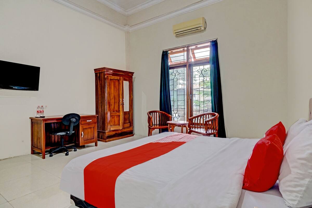 A hotel room with a bed, a desk with a chair, a wardrobe, and a window with curtains.