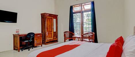 A hotel room with a bed, a desk with a chair, a wardrobe, and a window with curtains.