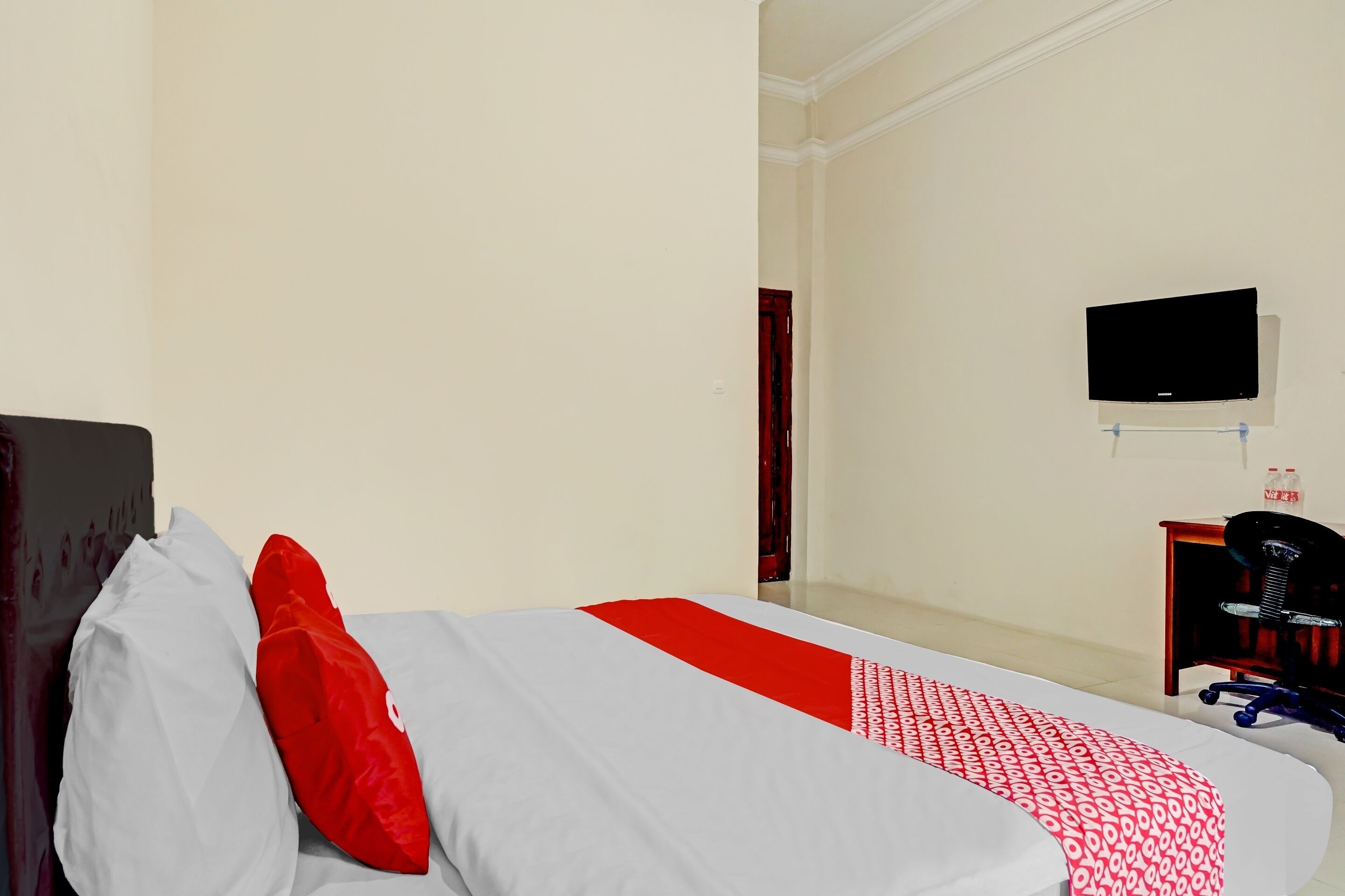A hotel room with a bed, a TV mounted on the wall, and a desk with a chair.