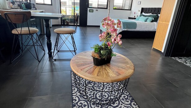 A spacious living area with a round coffee table, a sofa, and a dining table with chairs. There is a potted plant on the coffee table and a patterned rug on the floor. - Oasis Loft 5min from SJO airport cozy and comfy fully equipment  down town A/C (Alajuela)