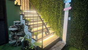 A staircase with a metal railing leading up to a wall covered in green foliage. There are signs indicating a welcome to the garden and a motel with vacancies. - Oasis Loft 5min from SJO airport cozy and comfy fully equipment  down town A/C (Alajuela)