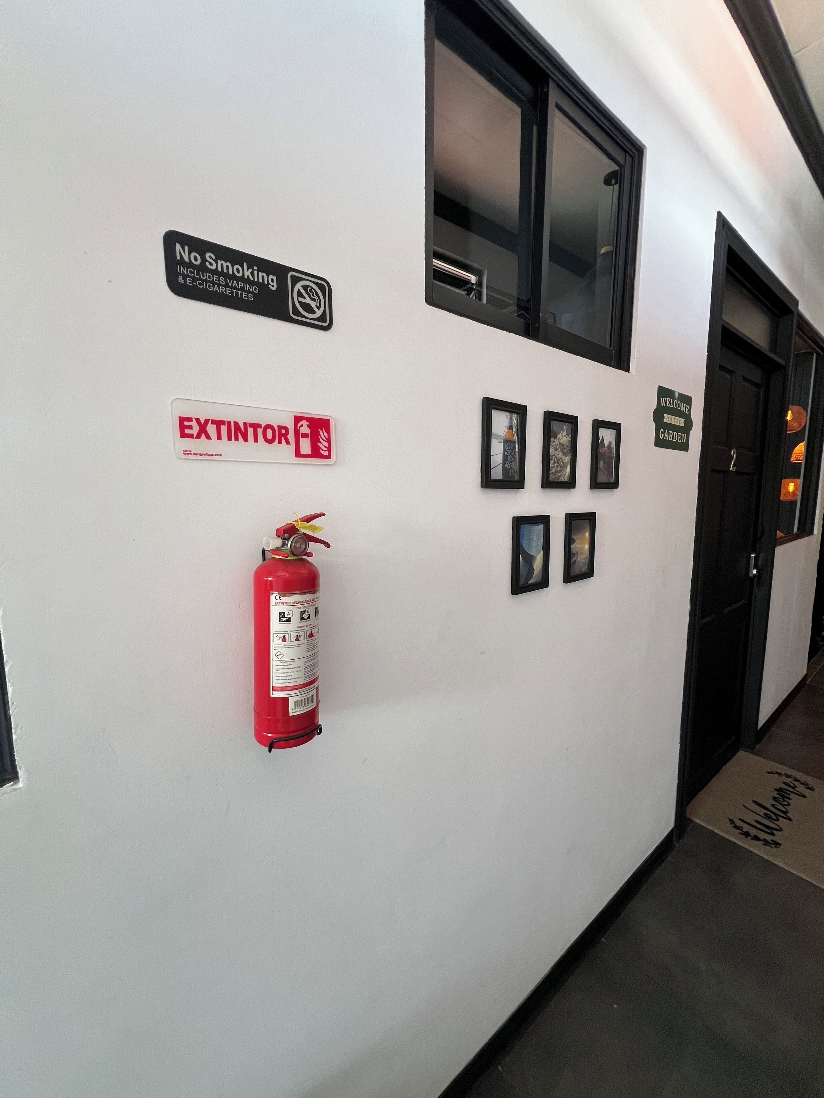 A hallway with a fire extinguisher, a no smoking sign, an extinguisher sign, and framed pictures on the wall.