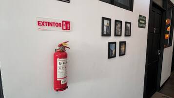 A hallway with a fire extinguisher, a no smoking sign, an extinguisher sign, and framed pictures on the wall.