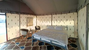 A tented room with a bed, a chair, and a small table. - DESERT INN CAMP (Bhuj)