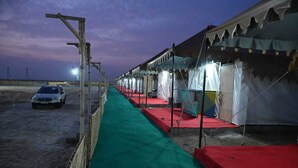 A row of tents with red and green flooring, a car parked outside, and a clear sky. - DESERT INN CAMP (Bhuj)