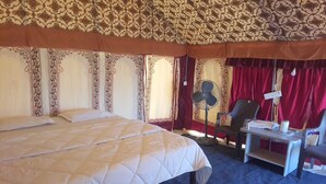 A hotel room with a large bed, a desk with a chair, a fan, and a red curtain. - DESERT INN CAMP (Bhuj)