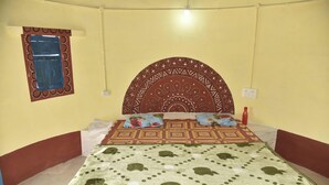 A room with a bed, a patterned headboard, a window with tape, and a wall socket. - DESERT INN CAMP (Bhuj)