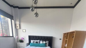 Un dormitorio moderno con cama, un banco, armario y lámparas colgantes.