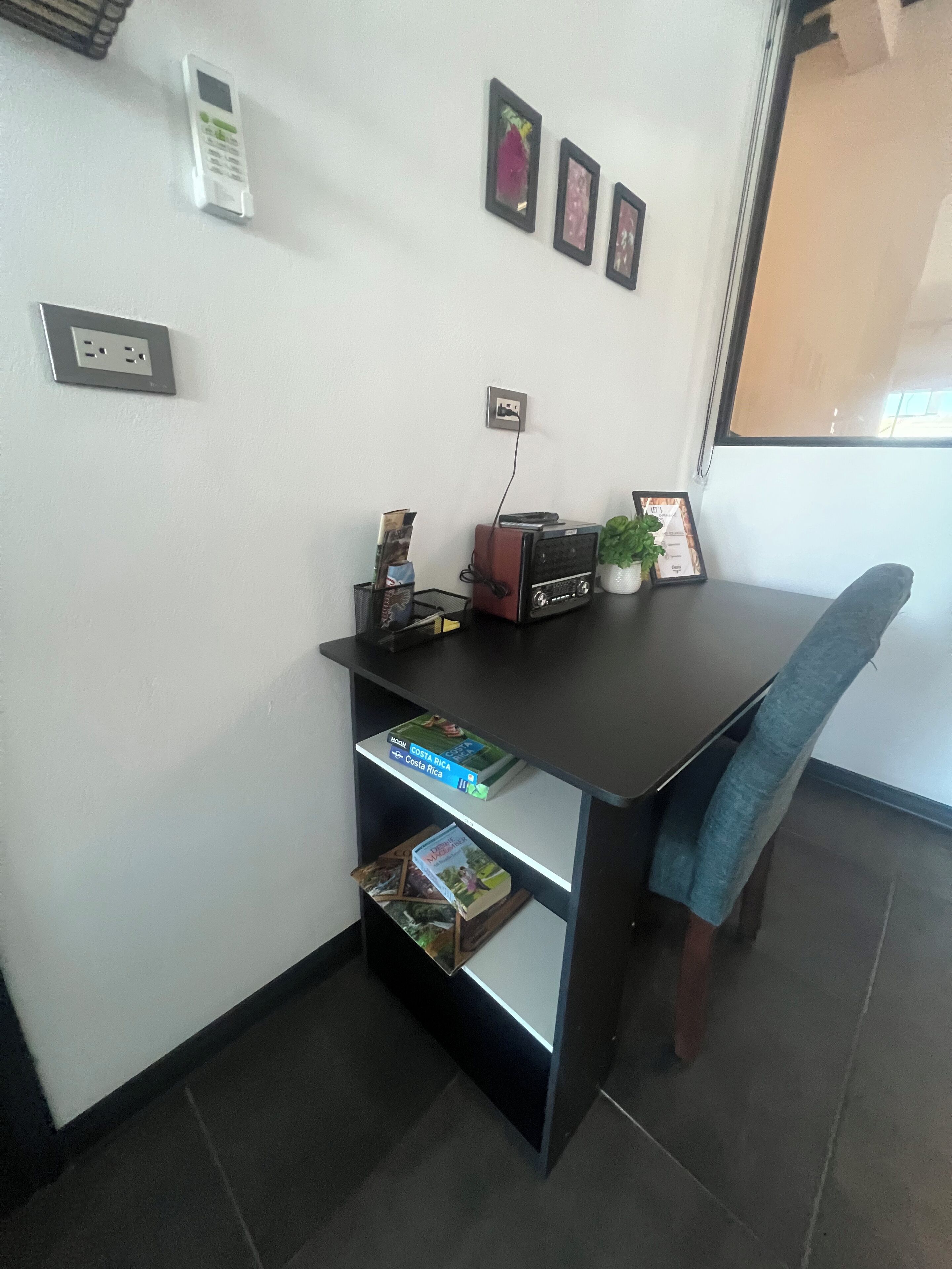 Un petit bureau comprenant un bureau, des étagères, une chaise, une plante en pot et des tableaux encadrés accrochés au mur.