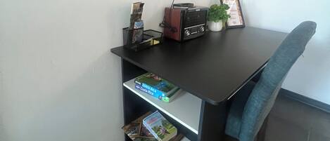 Un petit bureau comprenant un bureau, des étagères, une chaise, une plante en pot et des tableaux encadrés accrochés au mur.