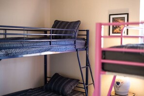 Una cama litera con colchón y almohadas, un cuadro enmarcado en la pared y una mesita con un objeto decorativo.