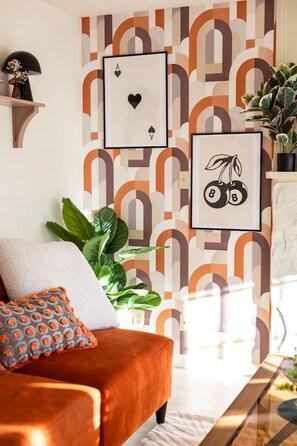 Ein Wohnzimmer mit ornamentalem Wandpapier, einer Couch, einer Pflanze und gerahmten Bildern an der Wand.