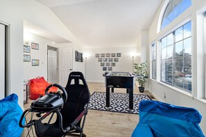 Ein Zimmer mit einem Kicker, einem Gaming-Sessel, einem blauen Sofa und einem Fenster mit Blick auf die Straße.