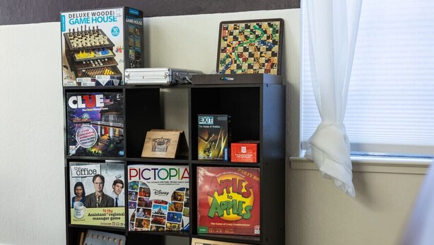 A shelf with various board games and a checkers board. - FunStation: 2800sqft Reno Getaway for All Ages (Sparks)