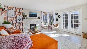 A living room with a fireplace, orange sofa, and a large window. - FunStation: 2800sqft Reno Getaway for All Ages (Sparks)