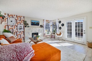 Una sala de estar con chimenea, sofá naranja y un ventanal grande.