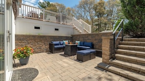 An outdoor patio with a stone wall, a staircase, and a seating area with a table and chairs. - Classic Renovated Cape Cod Getaway (Falmouth)