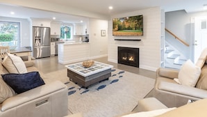A modern living room with a fireplace, a dining area, and a kitchen. - Classic Renovated Cape Cod Getaway (Falmouth)