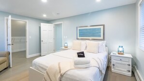 A bedroom with a bed, bedside tables, a nightstand, a chair, and a door to another room. - Classic Renovated Cape Cod Getaway (Falmouth)