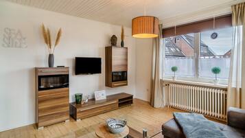 Ein modernes Wohnzimmer mit Flachbildfernseher, Holzmöbeln, einem Glastisch und Blick ins Freie.