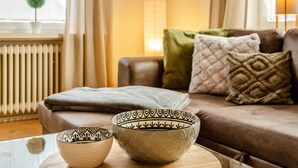 Uma sala de estar com um sofá marrom, almofadas estampadas, uma mesa de centro de vidro e duas peças decorativas.