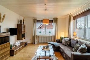 A modern living room with a sofa, coffee table, TV, and a window with curtains.
