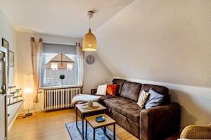 A cozy living room with a brown sofa, a small table, a lamp, and a view of a building through a window.