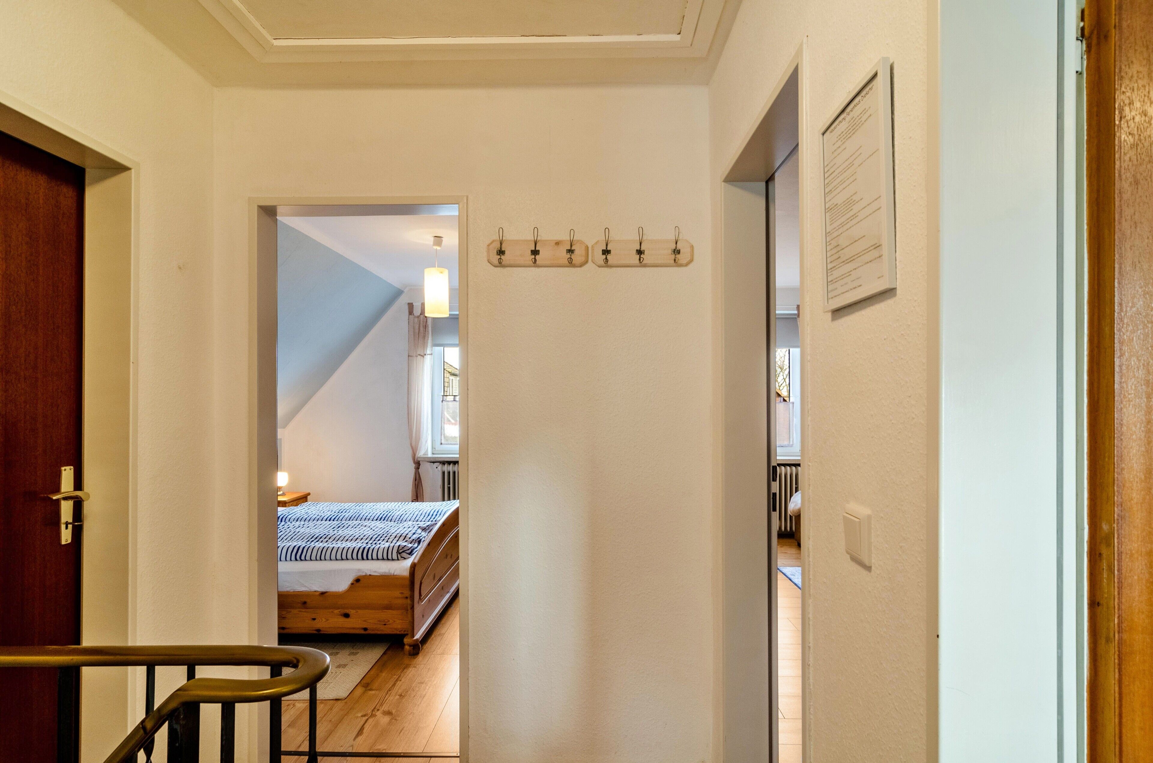 Un couloir mène à une chambre à coucher qui contient un lit, un plancher en bois et un plafond doté d’un luminaire.
