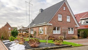 Ein Ziegelhaus mit geneigtem Dach, einem sichtbaren Schornstein und einem Garten mit Pflanzen und einem kleinen Baum.