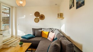 Ein modernes Wohnzimmer mit einem Ecksofa, einem kleinen Tisch, einer Pendelleuchte und Wandbildern.